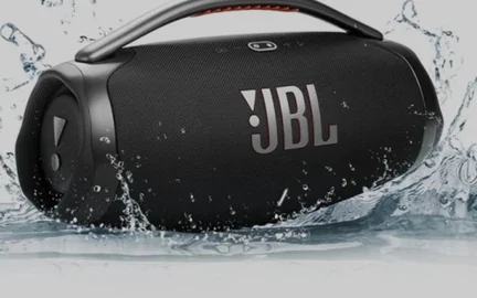 A cylindrical portable speaker photographed against a burst of splashing water