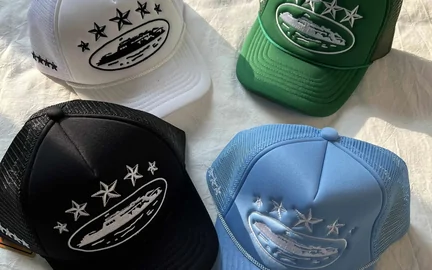 Four baseball caps in white, green, black and pale blue arranged face up on a table
