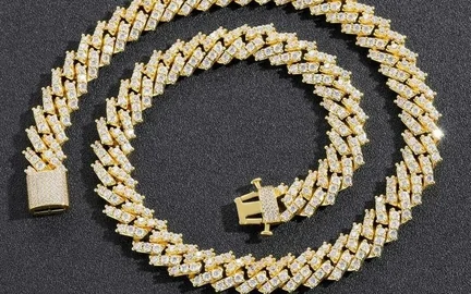 A gold-tone Cuban link chain coiled on a dark surface next to a matching pendant