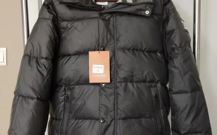 A black quilted puffer jacket laid flat on white, with an orange card tag still attached at the chest
