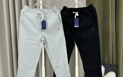 Grey and black joggers folded on a bed, each with a purple card tag still attached at the waistband